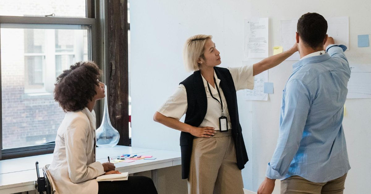 Three professionals in an office looking at information pinned to the wall